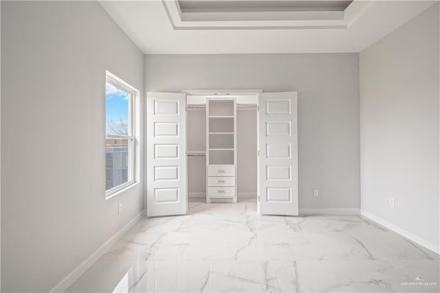 unfurnished bedroom with marble finish floor, a tray ceiling, and baseboards