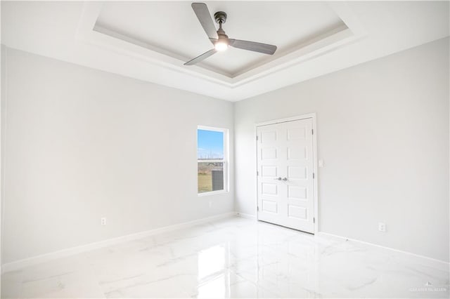 unfurnished bedroom with marble finish floor, a tray ceiling, and baseboards