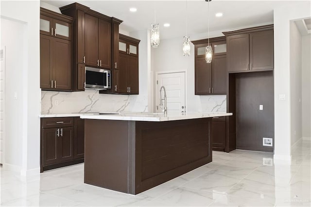 kitchen featuring marble finish floor, light countertops, stainless steel microwave, and glass insert cabinets