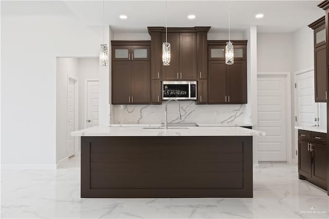 kitchen featuring marble finish floor, decorative light fixtures, stainless steel microwave, glass insert cabinets, and dark brown cabinetry