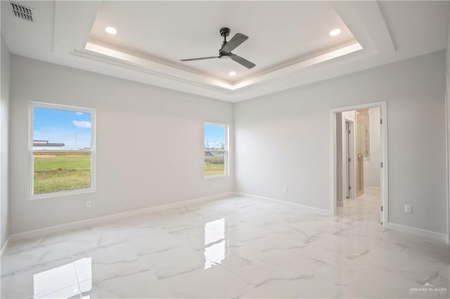 empty room with marble finish floor, a tray ceiling, visible vents, and baseboards