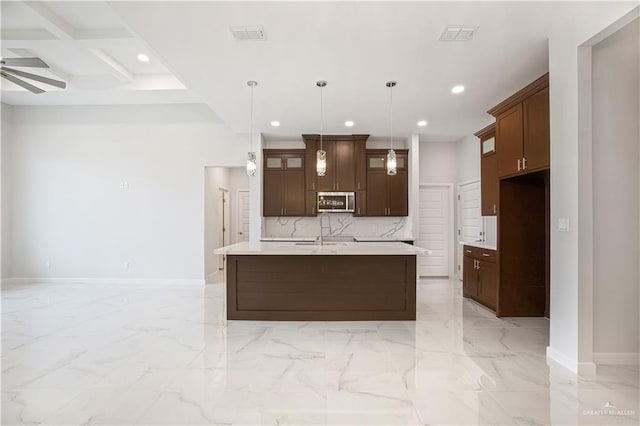 kitchen with marble finish floor, a kitchen island with sink, light countertops, and decorative light fixtures