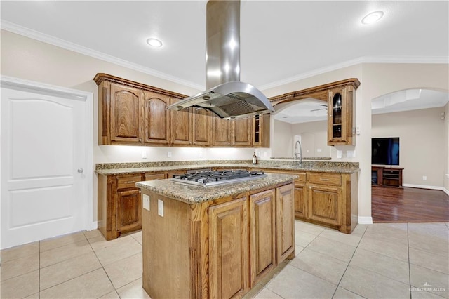 kitchen featuring light tile patterned floors, arched walkways, glass insert cabinets, island exhaust hood, and stainless steel gas stovetop