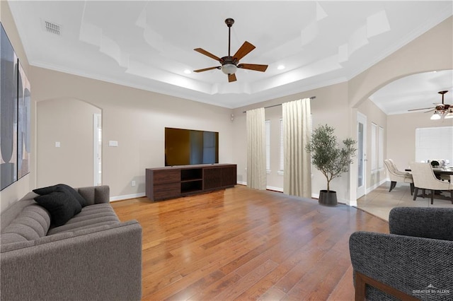 living room with a ceiling fan, arched walkways, visible vents, and a tray ceiling