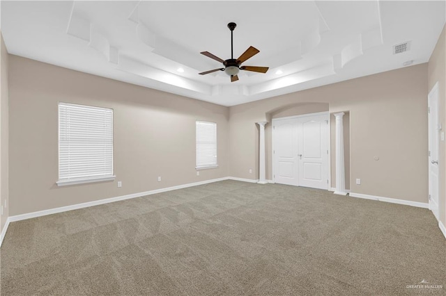 unfurnished bedroom with carpet flooring, visible vents, baseboards, a raised ceiling, and decorative columns