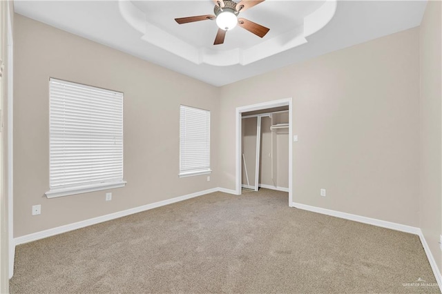 unfurnished bedroom with light colored carpet, a ceiling fan, baseboards, a closet, and a tray ceiling