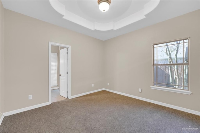 empty room with a raised ceiling, light carpet, and baseboards