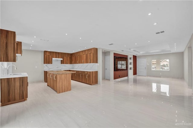 kitchen featuring visible vents, brown cabinetry, open floor plan, a center island, and a sink