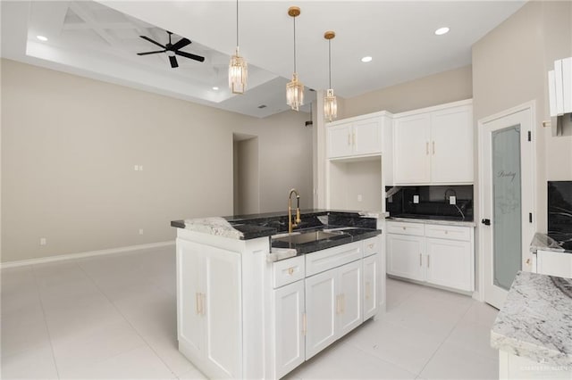 kitchen with sink, a tray ceiling, an island with sink, and white cabinets