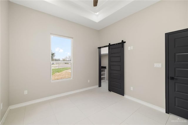 unfurnished room with a raised ceiling, a barn door, light tile patterned floors, and ceiling fan