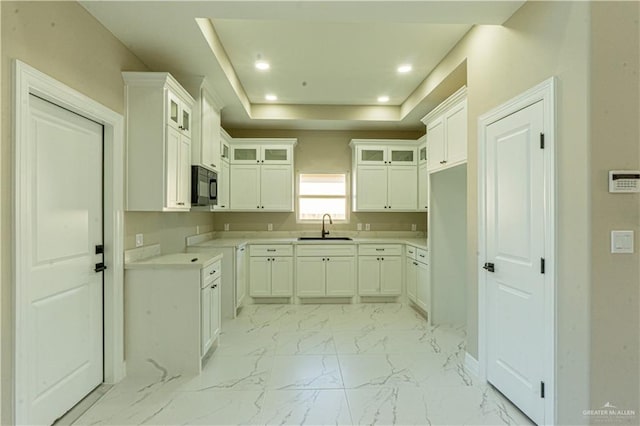 kitchen with marble finish floor, a raised ceiling, glass insert cabinets, a sink, and black microwave