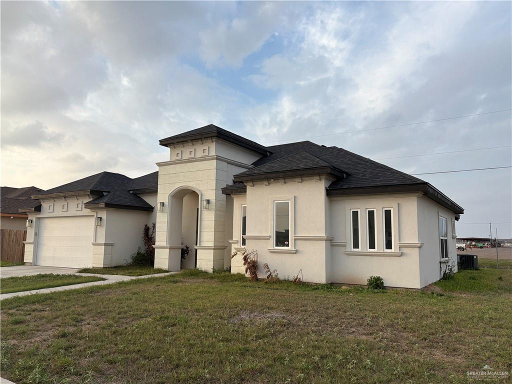 view of front of home featuring a garage, a shingled roof, concrete driveway, stucco siding, and a front yard