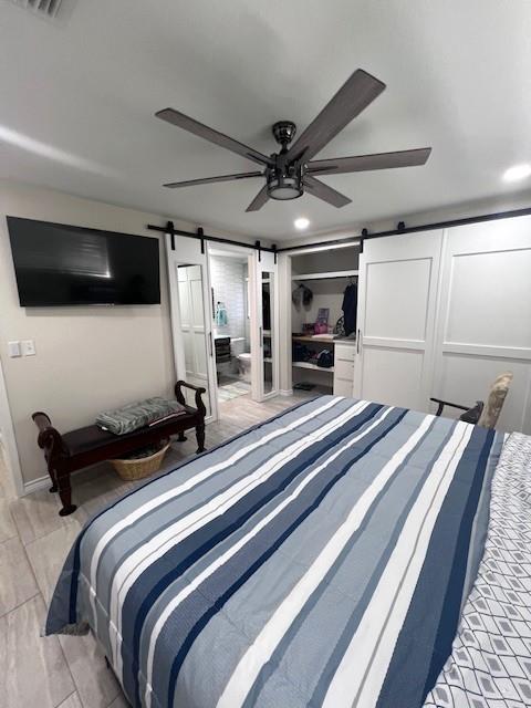 bedroom with a barn door, ceiling fan, and a closet