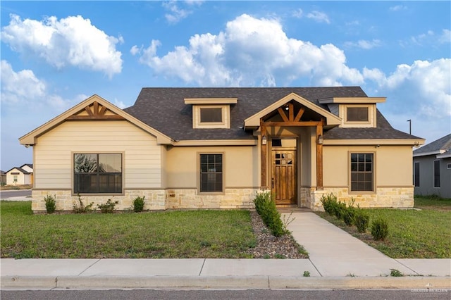 craftsman-style house with stone siding, roof with shingles, and a front yard