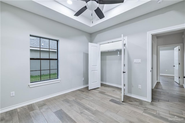unfurnished bedroom featuring light wood finished floors, baseboards, ceiling fan, and a raised ceiling