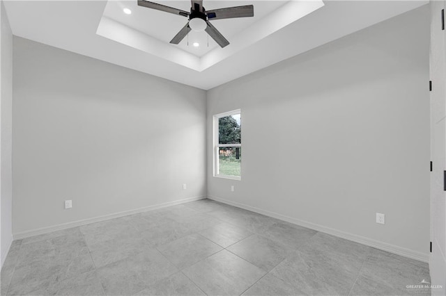 empty room with ceiling fan and a tray ceiling