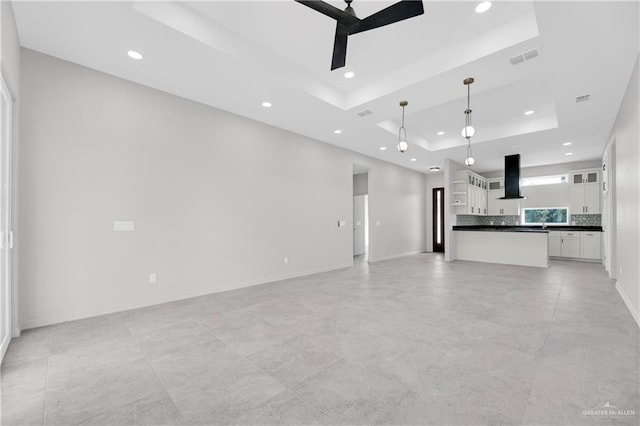 unfurnished living room featuring a raised ceiling and ceiling fan