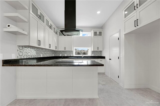 kitchen with island exhaust hood, white cabinets, kitchen peninsula, and dark stone countertops