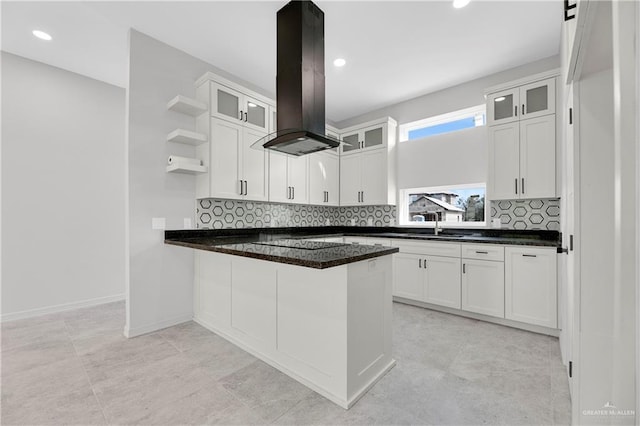 kitchen with dark stone counters, white cabinets, tasteful backsplash, island range hood, and kitchen peninsula