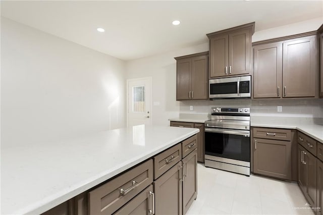 kitchen featuring dark brown cabinetry, decorative backsplash, light tile patterned flooring, and stainless steel appliances