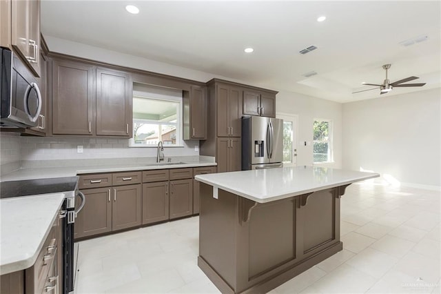 kitchen with tasteful backsplash, stainless steel appliances, ceiling fan, sink, and a kitchen island