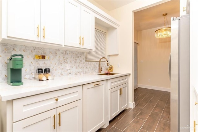 kitchen featuring stainless steel refrigerator, white cabinetry, sink, hanging light fixtures, and a notable chandelier