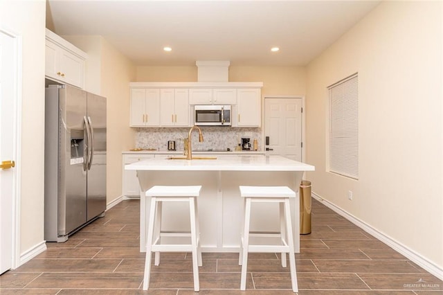 kitchen with a center island with sink, a kitchen breakfast bar, sink, appliances with stainless steel finishes, and white cabinetry