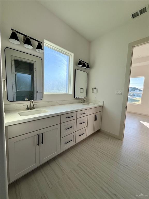 full bathroom with double vanity, visible vents, a sink, and wood finished floors