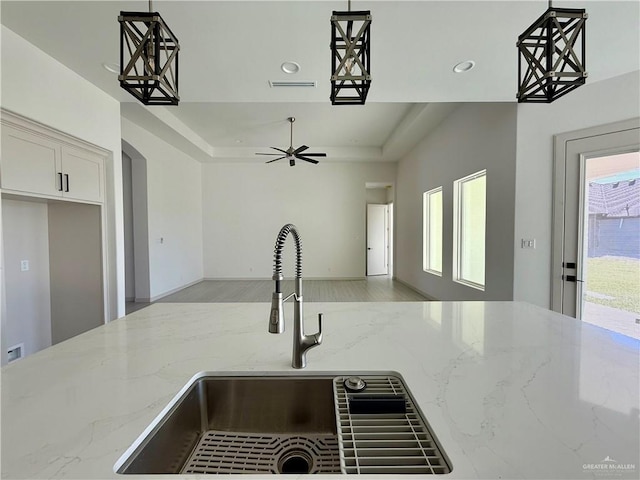 kitchen featuring light stone counters, a sink, visible vents, hanging light fixtures, and a tray ceiling