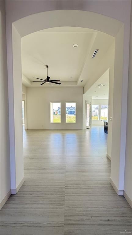 hall featuring arched walkways, light wood finished floors, visible vents, and baseboards