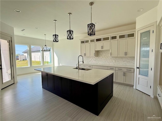 kitchen featuring glass insert cabinets, a sink, a kitchen island with sink, and white cabinetry