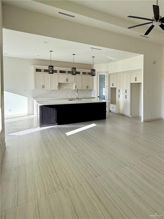 unfurnished living room featuring ceiling fan, a sink, visible vents, and baseboards