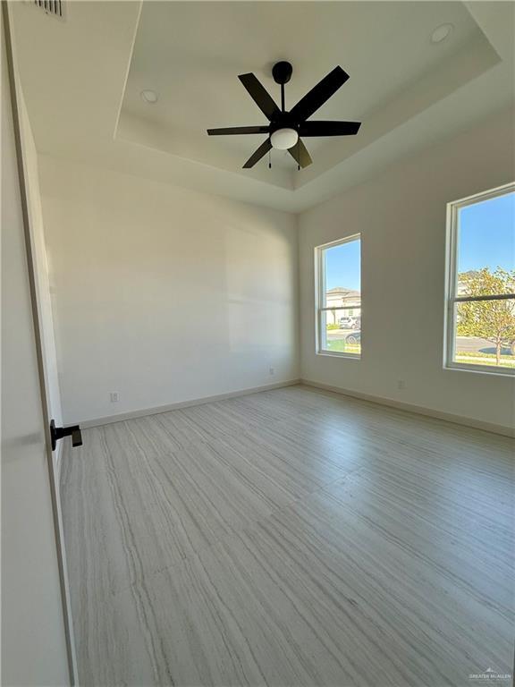 empty room featuring a tray ceiling, a ceiling fan, a wealth of natural light, and baseboards