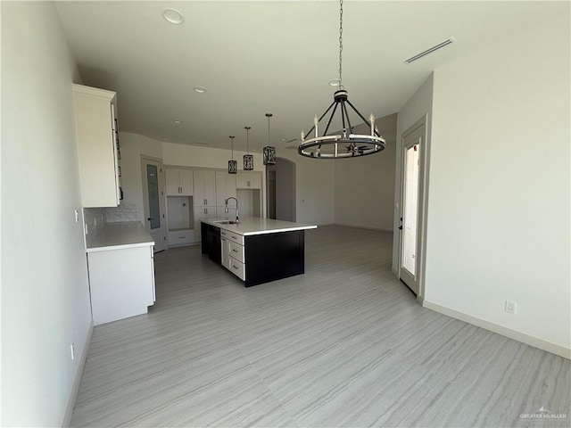 kitchen with a sink, visible vents, white cabinetry, light countertops, and a center island with sink