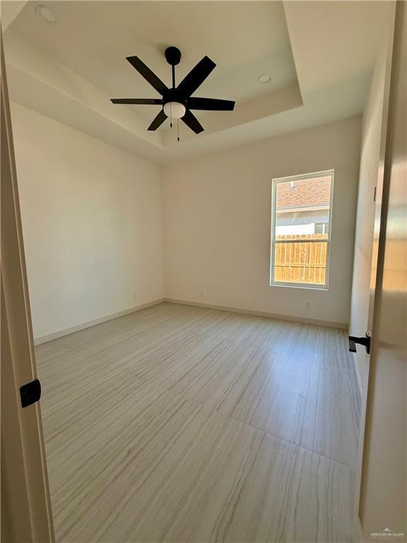 spare room featuring ceiling fan, light wood finished floors, a raised ceiling, and baseboards