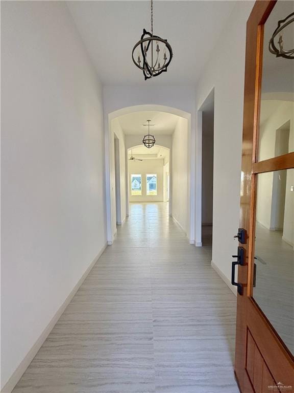 hall featuring light wood finished floors, baseboards, and arched walkways