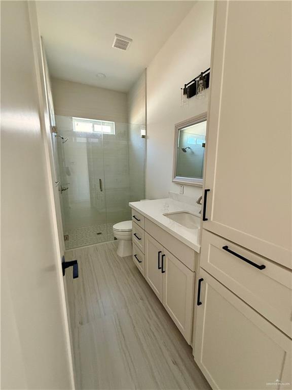 full bath featuring visible vents, toilet, a stall shower, vanity, and wood finished floors