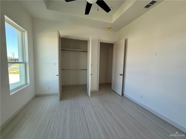 unfurnished bedroom featuring baseboards, visible vents, a raised ceiling, a ceiling fan, and light wood-style floors