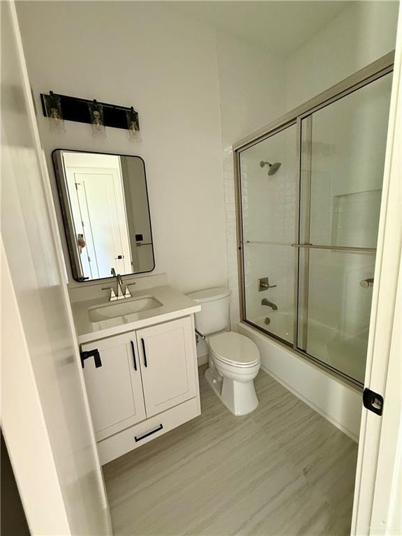 bathroom with toilet, shower / bath combination with glass door, wood finished floors, and vanity