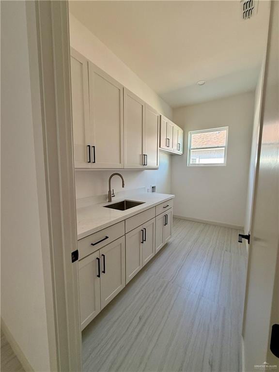 interior space with light countertops, light wood finished floors, a sink, and white cabinetry