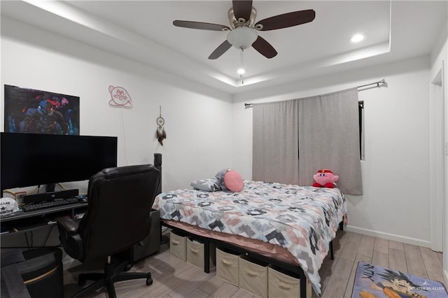 bedroom with a tray ceiling, recessed lighting, a ceiling fan, wood finished floors, and baseboards