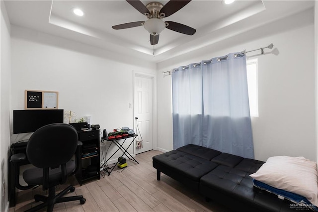 office area with light wood-style floors, a raised ceiling, and a ceiling fan