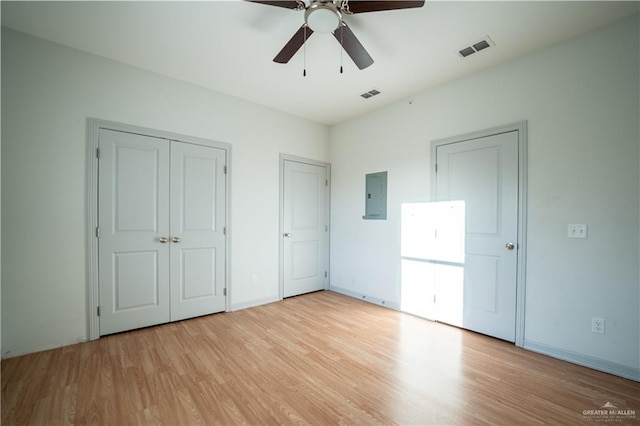 unfurnished bedroom with ceiling fan, light hardwood / wood-style floors, electric panel, and multiple closets