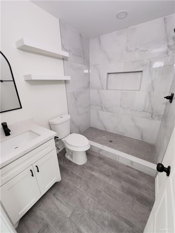 bathroom with toilet, a tile shower, hardwood / wood-style flooring, and vanity