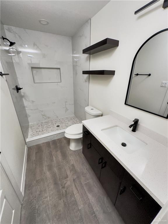 bathroom featuring toilet, a tile shower, and vanity