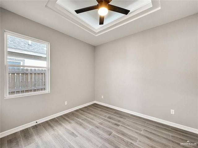 spare room with a tray ceiling, light hardwood / wood-style floors, and ceiling fan