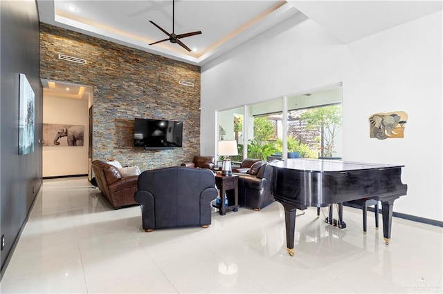 tiled living room with a raised ceiling, ceiling fan, and a high ceiling