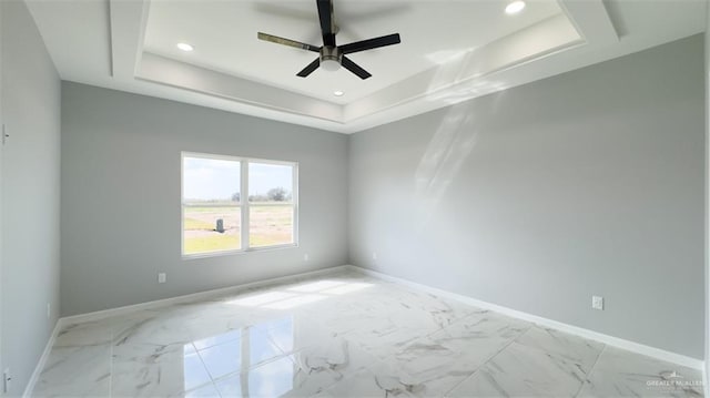 empty room with ceiling fan and a raised ceiling