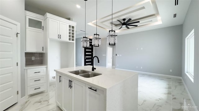 kitchen featuring an island with sink, white cabinets, decorative light fixtures, a tray ceiling, and sink