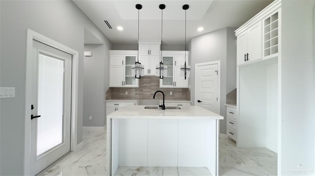 kitchen with tasteful backsplash, white cabinets, pendant lighting, sink, and a kitchen island with sink